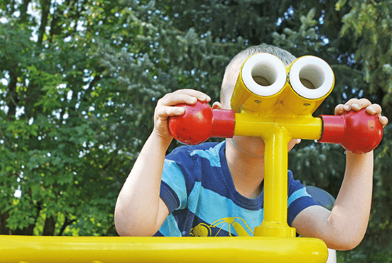 In einer Kindertagesstätte schaut ein Junge durch ein gelbes Fernrohr.